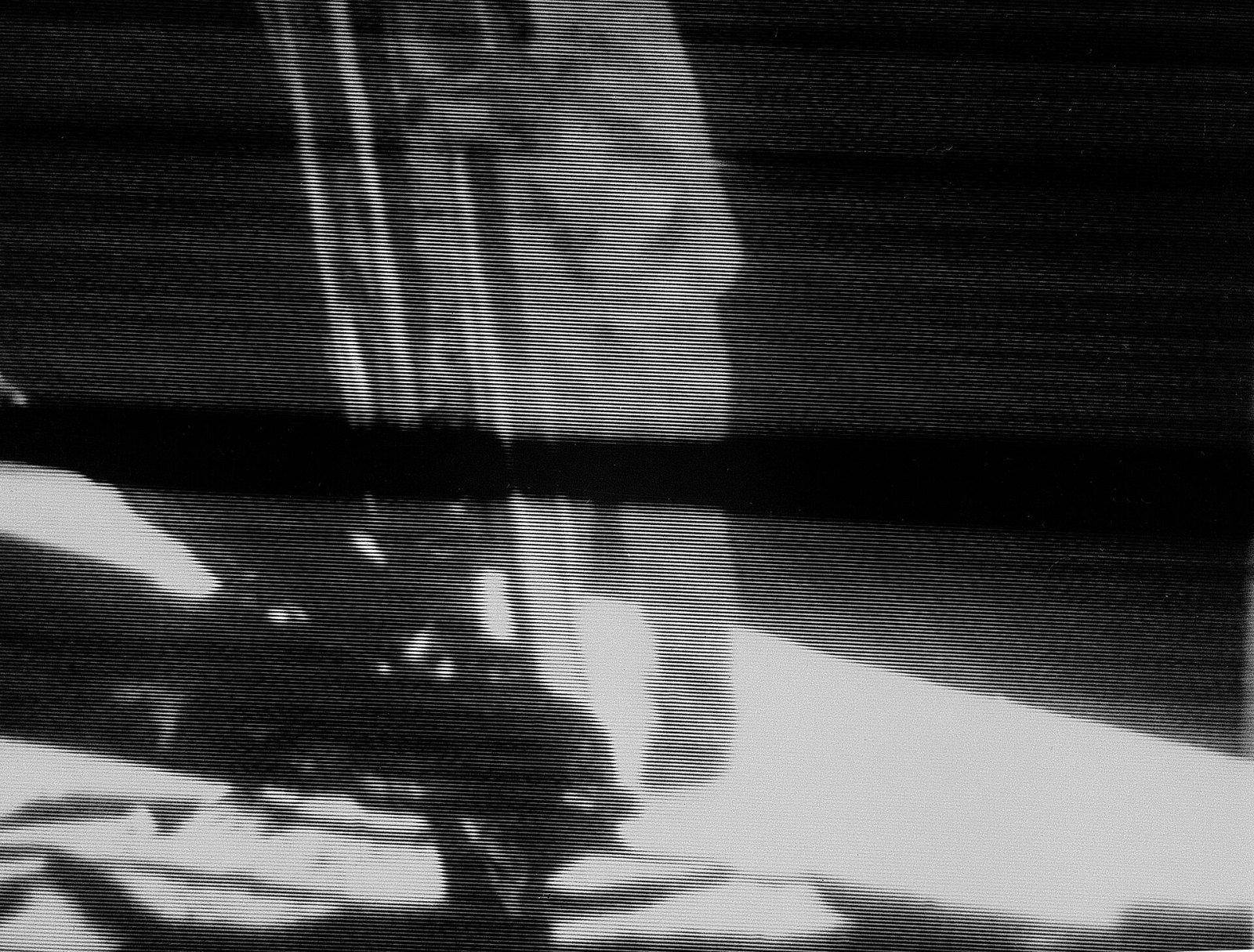 Grainy black-and-white television frame of Neil Armstrong descending the lunar module ladder, with a dark bar across the image